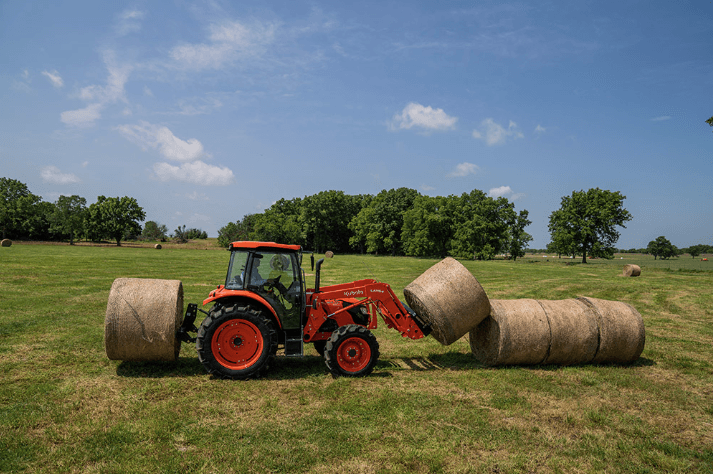 Man using Kubota utility tractor to move hay bales with front and rear attachments